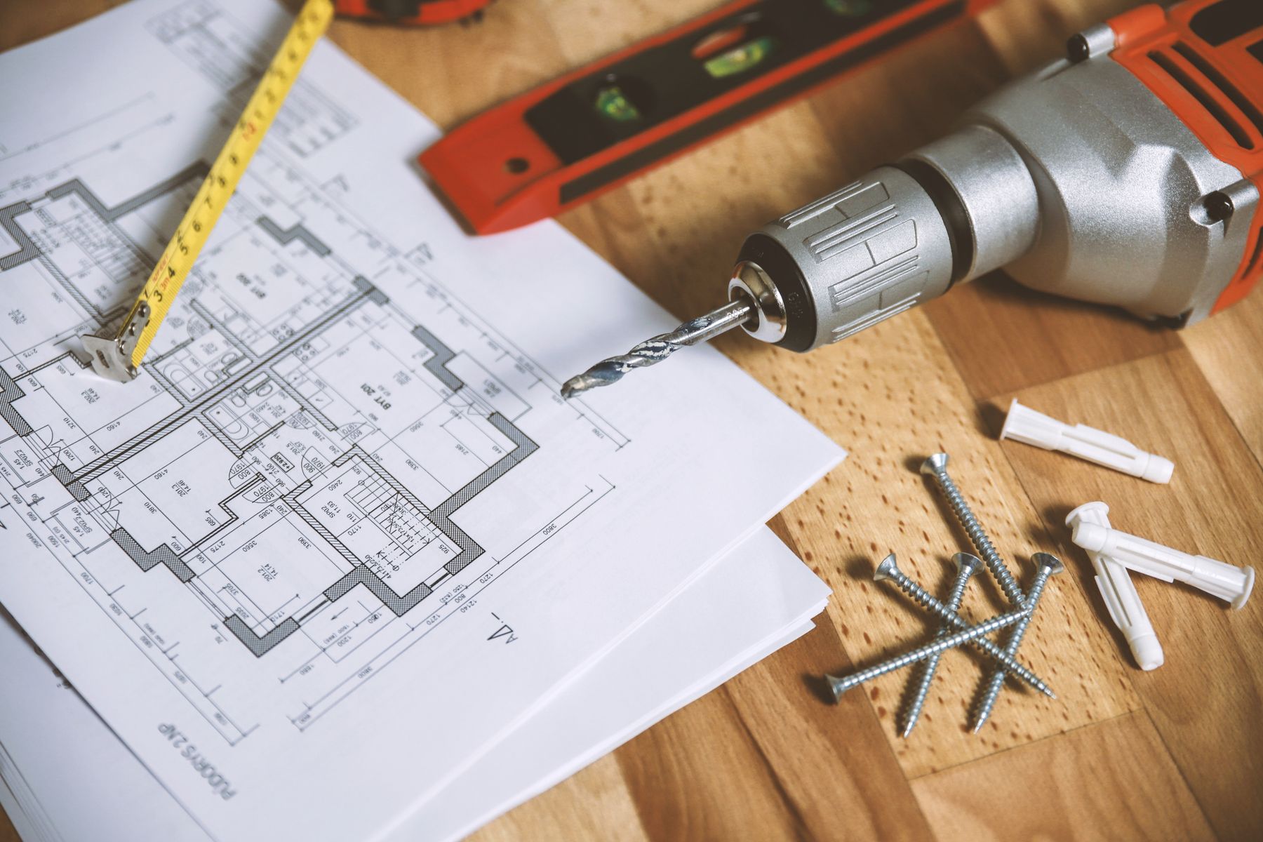 House plans with a level, drill, and fasteners on a workbench